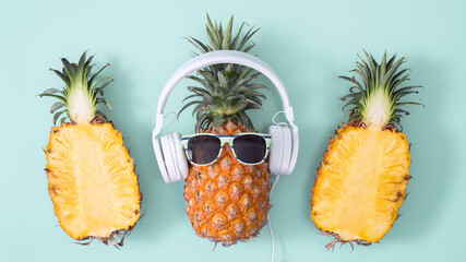 Funny pineapple wearing white headphone, concept of listening music, isolated on colored background with tropical palm leaves, top view, flat lay design.