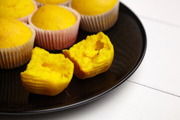 Muffins on black plate on white wooden table. Halved pumpkin cupcake. Homemade bakery, flour product