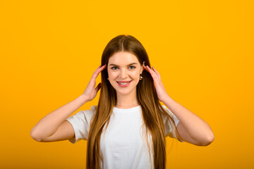 Isolated portrait of happy woman has toothy smile, closes eyes, feels pleasure from compliment, stands over yellow wall. Positive emotions and feelings concept