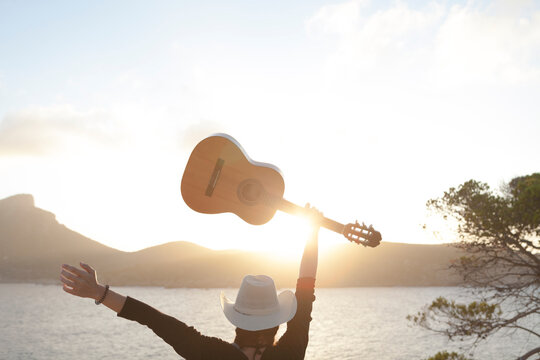 Arafed woman with guitar and hat standing on a cliff overlooking the ocean, by James Baynes, holding a guitar, women playing guitar, white straw flat brimmed hat, white cowboy hat, alan jackson