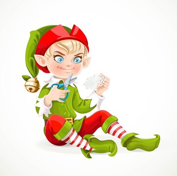 Cute boy elf sitting on the floor and cuts out a snowflake from a paper isolated on white background