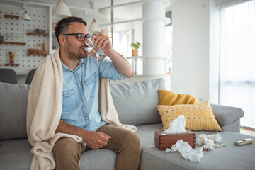 Cropped shot of a young man suffering with flu while sitting wrapped in a blanket on the sofa at home. It's the season of sneezes. Ill man covered with blanket.