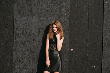 Red-haired girl in a black dress near a dark textured wall
