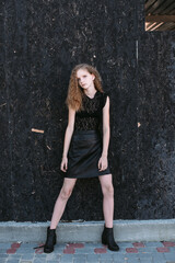 Red-haired girl in a black dress near a dark textured wall