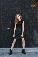 Naklejka premium Red-haired girl in a black dress near a dark textured wall