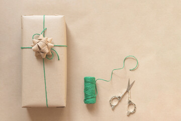 present wrapped in plain recycled paper with green thread and scissors on beige background
