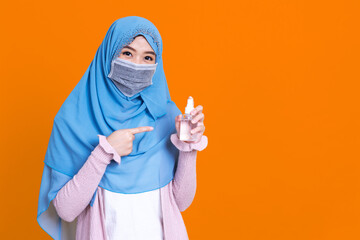 Muslim asian woman with traditional dress wearing medical face mask under the outbreak of the virus,Wash her hands with an alcohol gel isolated on color background