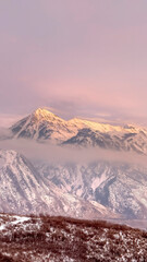 Fototapeta na wymiar Vertical frame Snowy Wasatch Mountain and hill top towering over Utah Valley under cloudy sky