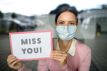 Portrait of teacher with face mask after lockdown, holding miss you sign.