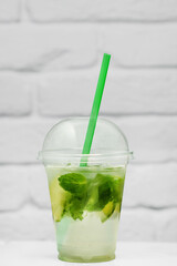 summer refreshing lemonade in a takeaway cup against a white brick wall