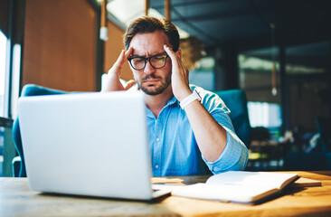 Obraz premium Businessman feeling headache while doing distance work in coffee shop