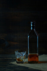 Alcohol in a glass with ice and bottles placed beside the wooden floors and the backdrop.