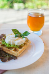 Healthy breakfast on a terrace with Viennese waffles and poached egg with green salad and orange juice.