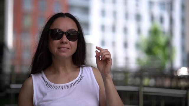 charming middle aged woman with sunglasses on street of city, flirting with camera