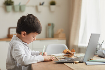 Warm-toned side view portrait of cute boy doing homework while sitting at desk in cozy interior, copy space