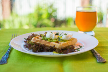 Healthy breakfast on a terrace with Viennese waffles and poached egg with green salad and orange juice.