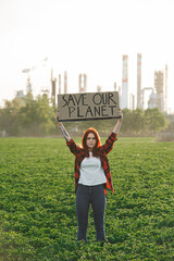 Young woman activist with placard standing outdoors by oil refinery, protesting.