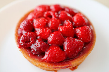 Fresh and red raspberry made a round tart. Close  view on a white plate. Wooden table background.