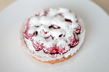 Raspberry tart covered with icing sugar on a white plate. 