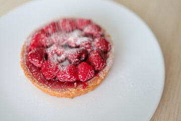 Sprinkle powdered sugar on a raspberry tart.