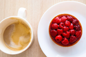 A raspberry tart on a white plate and a cup of coffee latte on the wooden table.