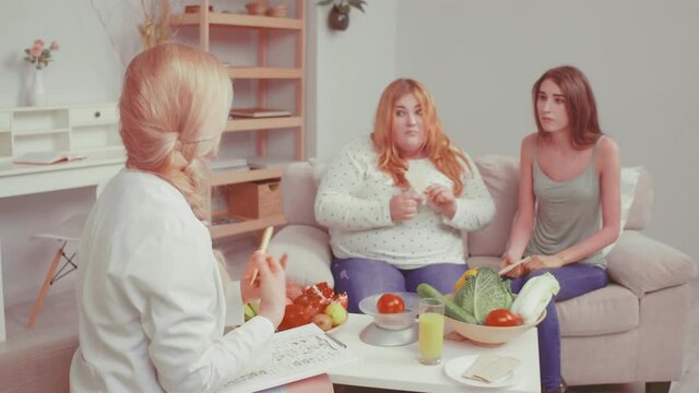 Bulimic and overweight girl trying bread rolls. Doctor talking about weight problem and consults about health issues with her friend girls. Healthy food concept. Tinted video. Prores 422. 