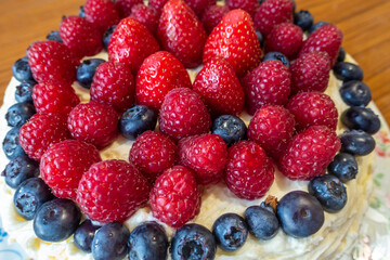 A cake decorated with butter icing and summer fruits including strawberries, raspberries and blueberries.