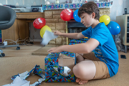 A Boy Sits On The Floor Unwrapping A Birthday Present, Tearing Off The Wrapping Paper Enthusiastically.