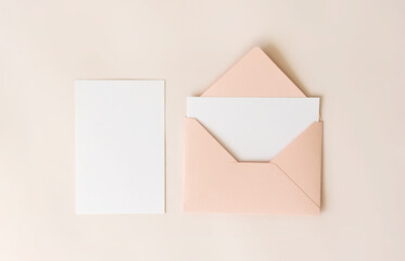 Mockup blank letter inside pink envelope and white paper on beige background, top view. Greeting card concept. Wedding invitation template
