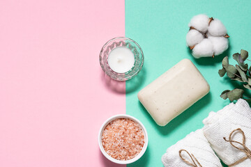 Spa and wellness concept. Rolled towels, Himalaya salt, natural soap, aromatic candle and decor on two tone background with copy space for your design.