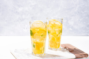 Citrus lemonade or mojito cocktail with lemon and orange and basil. Cold beverage or drink with ice on marble cutting board