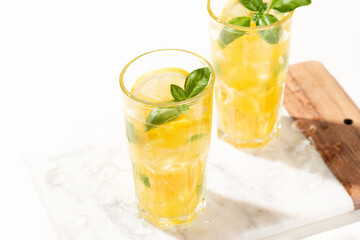 Citrus lemonade or mojito cocktail with lemon and orange and basil. Cold beverage or drink with ice on marble cutting board