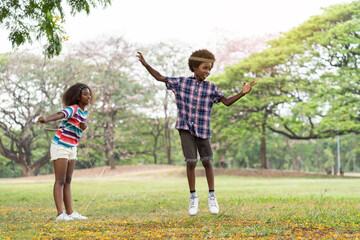 Happy young boy and girl paying in the park. Two African American children having fun with jumping over the rope in the garden. Education or Field trip concept