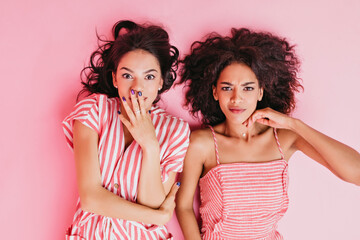 Photo on isolated pink background in studio. Two girls with beautiful tan and dark curly hair lie...