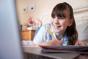 Young Girl Lying On Bed In Bedroom With Laptop Studying And Home Schooling