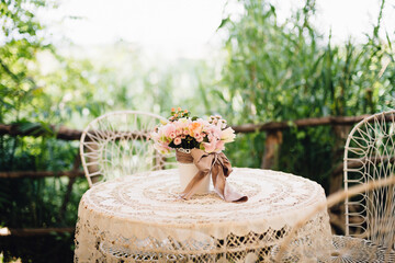 Open air rustic wedding in Italy. Wedding decor details. White chairs and table with flower composition.