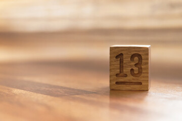 Number thirteen on wooden cube label on wooden table with shades of light through the window. Copy space