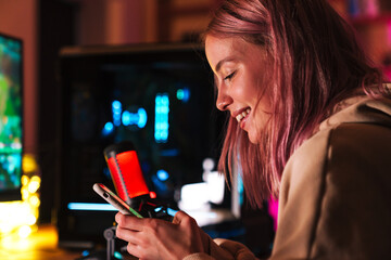 Image of girl using cellphone and smiling while playing video game