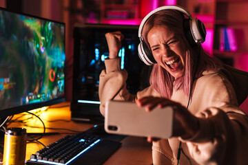 Image of girl taking selfie on cellphone while playing video game