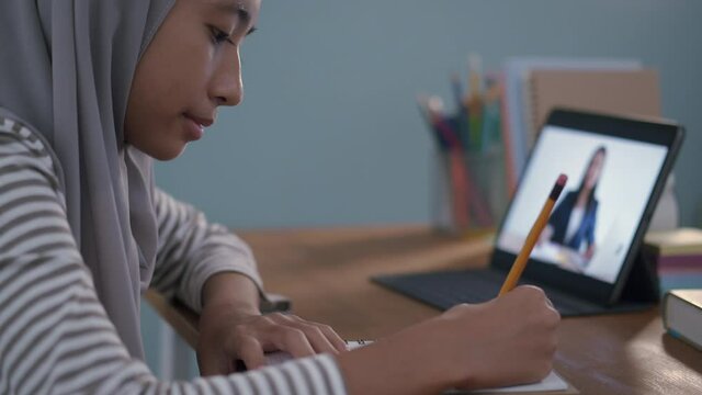 homeschooling. Muslim girl is studying online on tablet at home night
