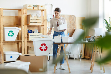Young woman doing recycling in warehouse she sorting garbage into the containers