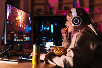 Image of delighted cute girl eating chips while playing video game