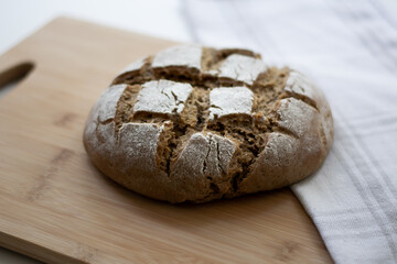 Homemade yeast sourdough rye wholegrain bread with Diamond Crosshatch scoring pattern on a wooden board with a kitchen towel. A dark and moody rustic atmosphere