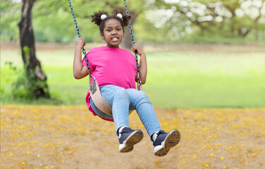 Cute African American little girl playing on swing. Smiling child playing in summer in the park. Kid in the field trips outdoor, Freedom, Happy lifestyle, Summer outdoor.