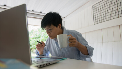 man holding coffee of white cup and working laptop on desk work at the home office