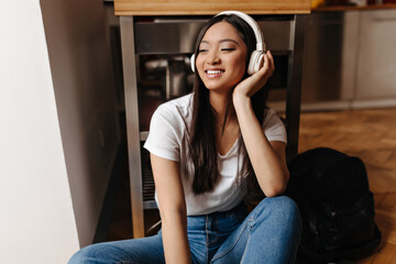 Adorable girl in white headphones posing with smile on floor in kitchen