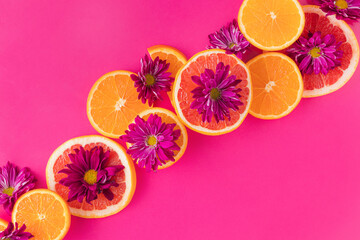 Colorful pattern made of slices of citrus fruits (orange, grapefruit) with purple flowers  in a fucsia background