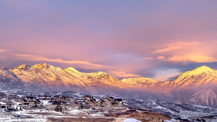 Fototapeta na wymiar Panorama Homes on snowy hill against frosted Wasatch Mountain with golden glow at sunset