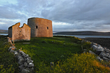 Ruines d'une tour et petite maison en pierre au bord de la mer, au coucher du soleil, en Irlande.