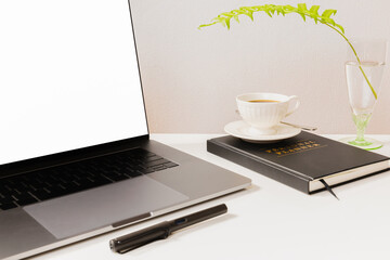 Mockup of laptop and pen with coffee cup over notebook on white table.